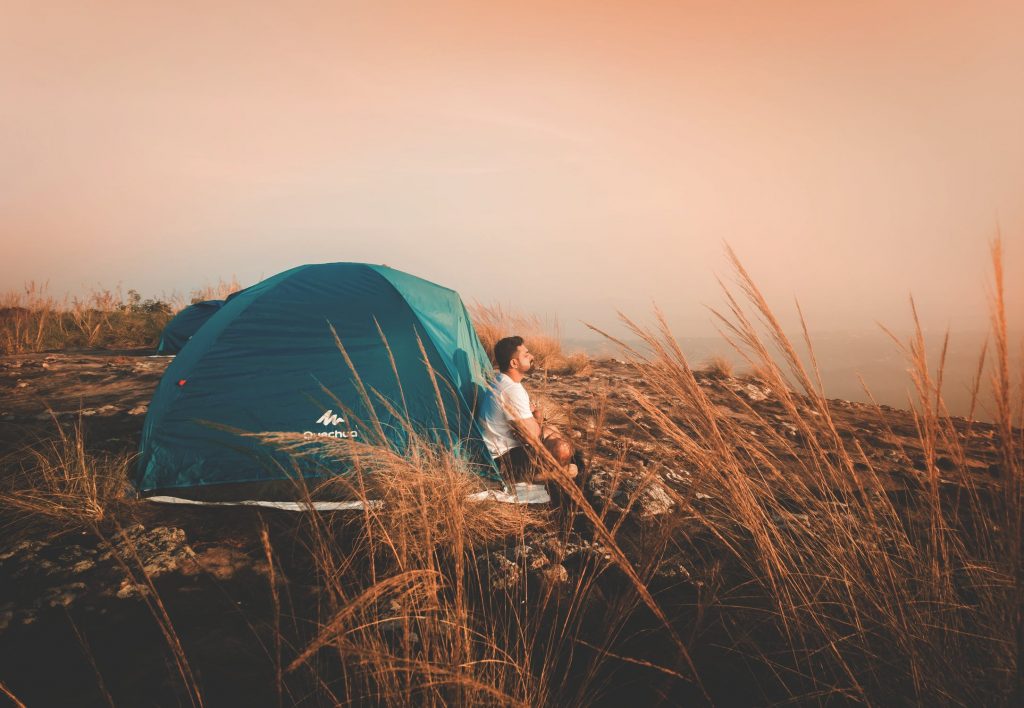 man sitting outside tent at sunset